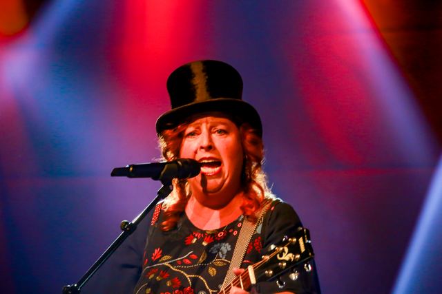 Sängerin mit Zylinder und Gitarre singt in rotem Bühnenlicht