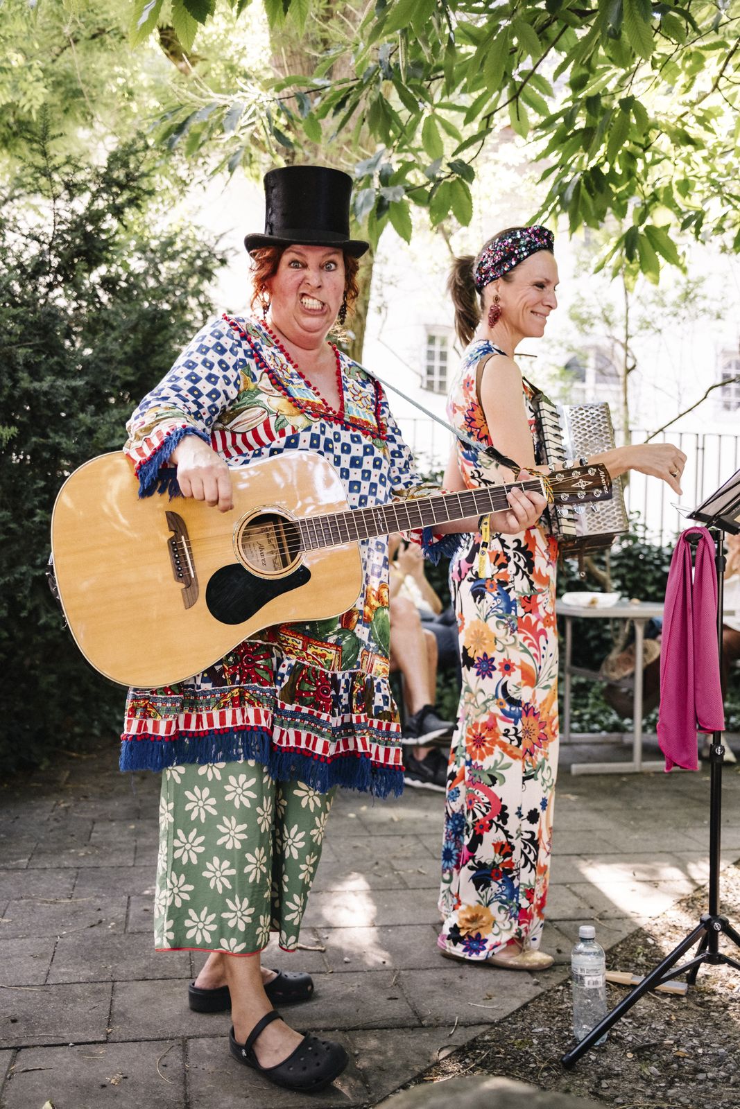 Die zwei Schrullen bei den Street Music Nights der Bandunion im Sommer 2025: eine mit Zylinder und Gitarre schneidet eine Grimasse, die andere spielt Akkordeon