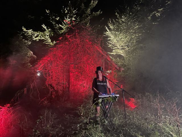 Musikerin am Keyboard vor einer rot beleuchteten Hütte bei Nacht, Videodreh